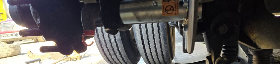 Underneath a truck, showing detailed work on the axle and brake components at Big Wheels Repair in Gainesville, highlighting heavy duty truck repair services