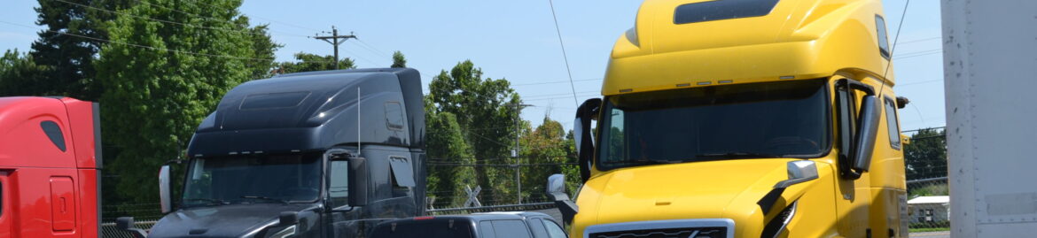 Parked heavy duty trucks, including a yellow and a black Volvo, at Big Wheels Repair in Gainesville, showcasing our repair and maintenance services.