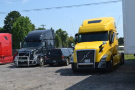 Parked heavy duty trucks, including a yellow and a black Volvo, at Big Wheels Repair in Gainesville, showcasing our repair and maintenance services.